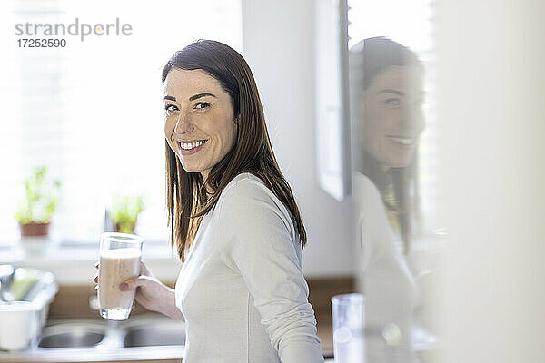 Frau lächelt und hält ein Glas Milchshake in der Küche