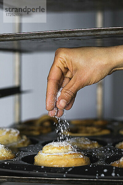 Hand streut Zucker auf Zimtschnecke in der Küche