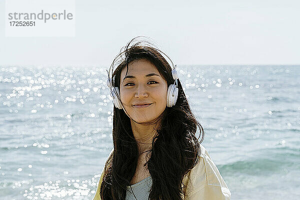 Schöne Frau mit In-Ear-Kopfhörern steht am Strand während des sonnigen Tages