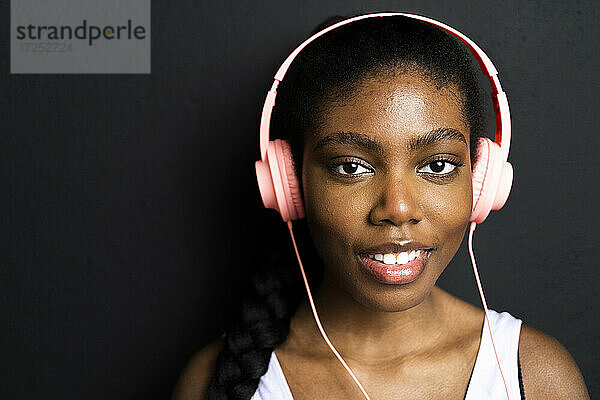 Lächelnde Frau hört Musik über Kopfhörer vor schwarzem Hintergrund