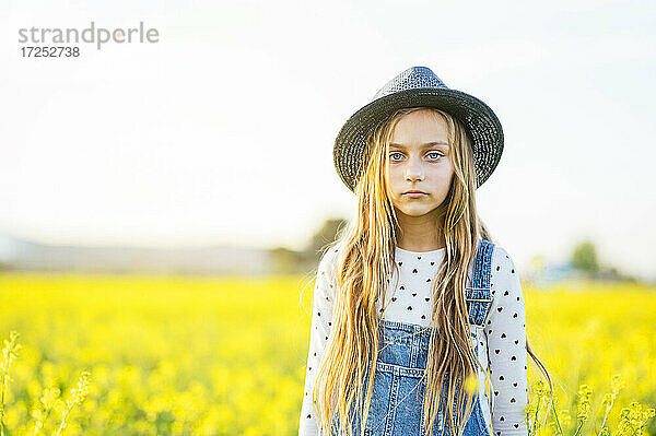 Blondes Mädchen mit Hut  das auf einem landwirtschaftlichen Feld steht
