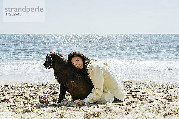 Frau umarmt Labrador-Hund im Sand am Strand