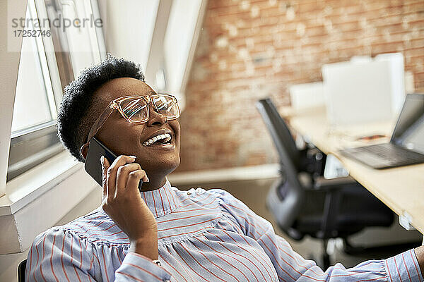 Glückliche Geschäftsfrau mit Brille  die im Büro mit einem Smartphone telefoniert