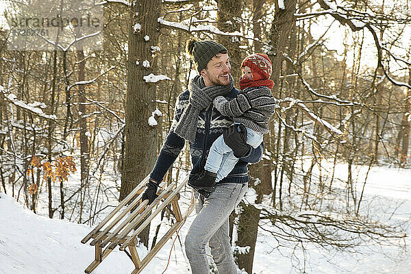 Vater mit Schlitten hält Sohn beim Winterspaziergang im Schnee