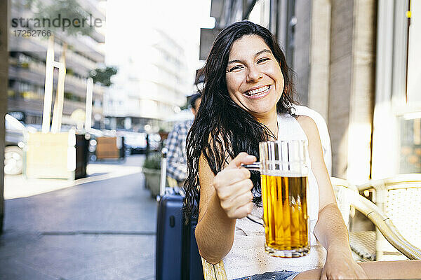 Lächelnde Frau hält ein Glas in der Hand  während sie im Biergarten sitzt