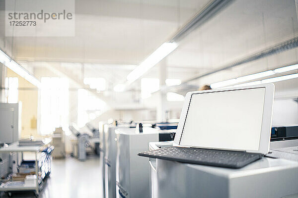 Digitales Tablet mit Druckmaschine im Hintergrund in einer Fabrik