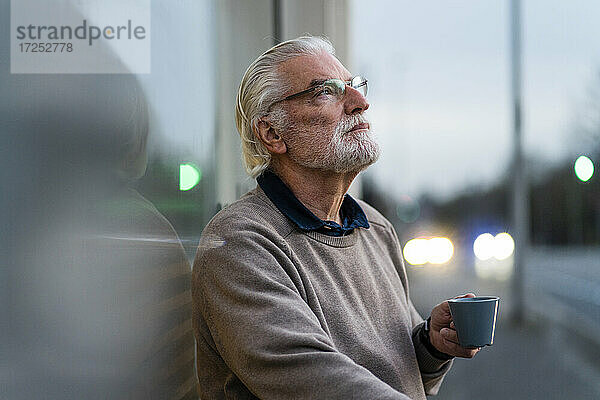 Nachdenklicher älterer Mann mit Kaffeetasse vor einem Straßencafé