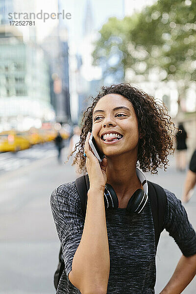 Junge Frau streckt die Zunge heraus  während sie in der Stadt mit einem Smartphone telefoniert