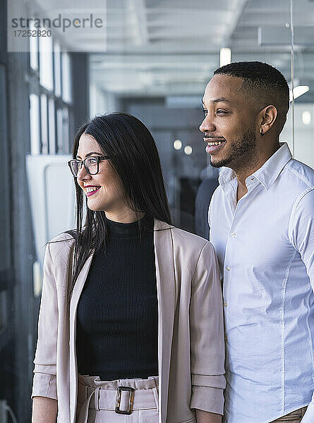 Lächelnde männliche und weibliche Unternehmer  die wegschauen  während sie in einem Coworking-Büro stehen