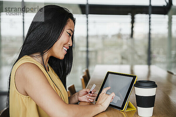 Unternehmerin beim Einkaufen mit Kreditkarte über ein digitales Tablet im Büro