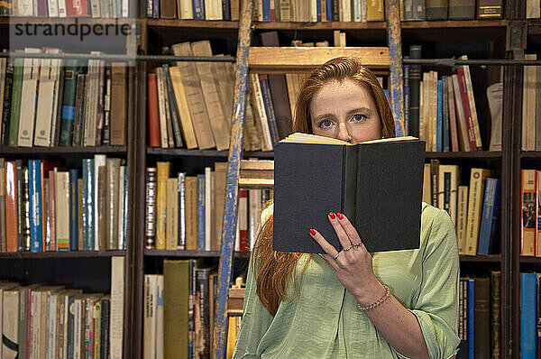 Junge Frau mit Buch auf Leiter in Bibliothek stehend