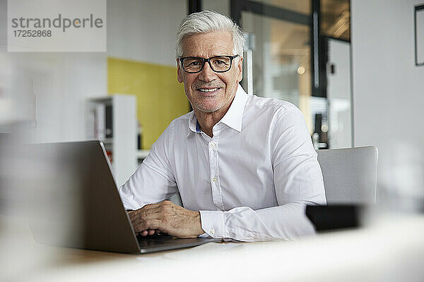 Älterer Unternehmer mit Laptop lächelnd im Büro