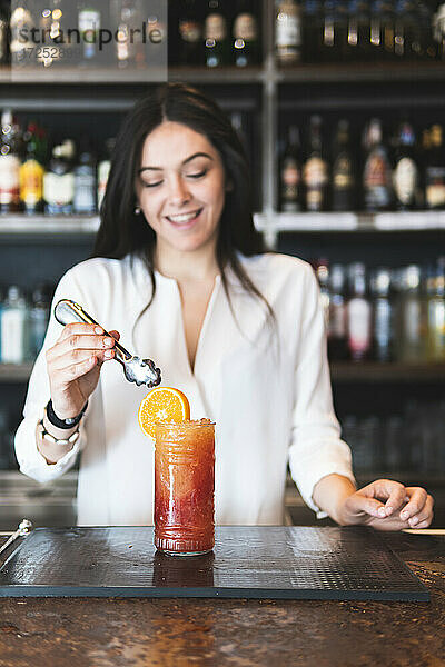 Lächelnde Barkeeperin serviert Cocktail am Tresen