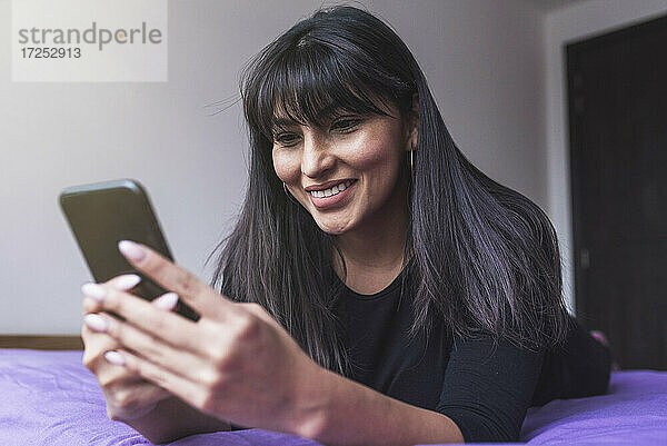 Schöne Frau mit Smartphone auf dem Bett