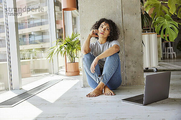 Junge Frau schaut weg  während sie in ihrer Wohnung auf dem Boden sitzt