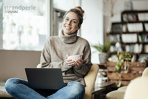 Geschäftsfrau mit Laptop  die lächelnd eine Schale in einem Café hält