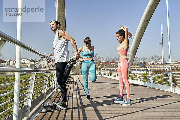 Multi-ethnische männliche und weibliche Athleten bei Übungen auf einer Brücke an einem sonnigen Tag