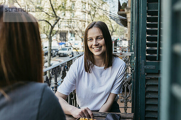 Lächelnde schöne junge Frau verbringt ihre Freizeit mit ihrer Freundin auf dem Balkon