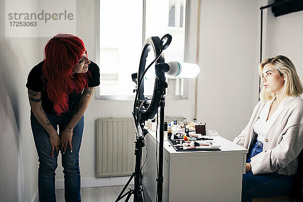 Lächelnde Make-up-Künstlerin betrachtet ein schönes Modell im Studio