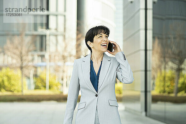 Lächelnde Geschäftsfrau  die in einem Büropark mit einem Mobiltelefon spricht