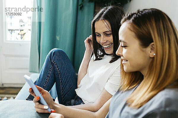 Lächelnde Frauen  die sich zu Hause ein Mobiltelefon teilen