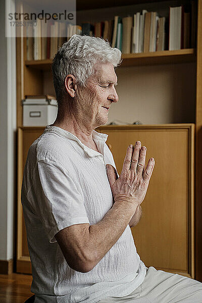 Mann mit gefalteten Händen beim Meditieren zu Hause