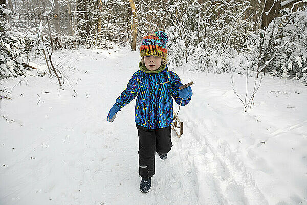 Niedlicher Junge  der im Winter einen Schlitten durch den Schnee zieht