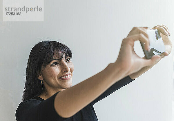 Lächelnde mittelgroße erwachsene Frau  die ein Selfie mit ihrem Mobiltelefon zu Hause macht