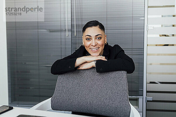 Lächelnde Geschäftsfrau lehnt auf einem Stuhl im Büro