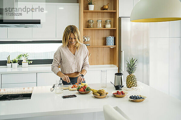 Lächelnde Frau  die an einer Kücheninsel Obst schneidet