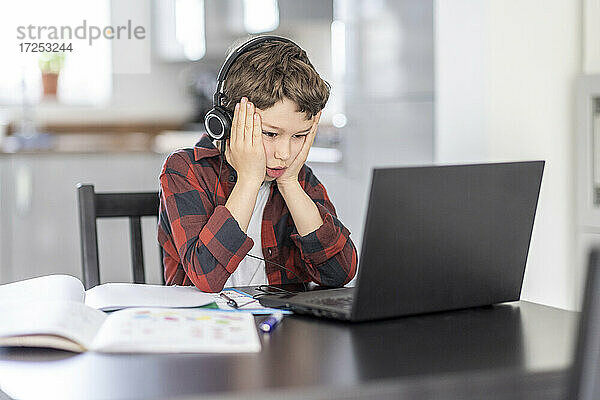 Junge mit Kopf in den Händen  der zu Hause am Laptop lernt