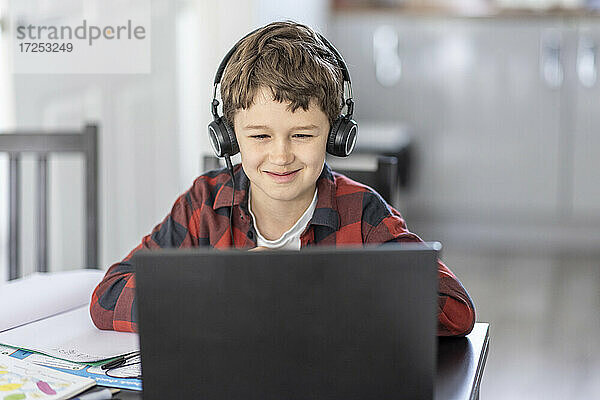 Lächelnder Junge  der über einen Laptop am Online-Unterricht teilnimmt  während er zu Hause e-Learning betreibt
