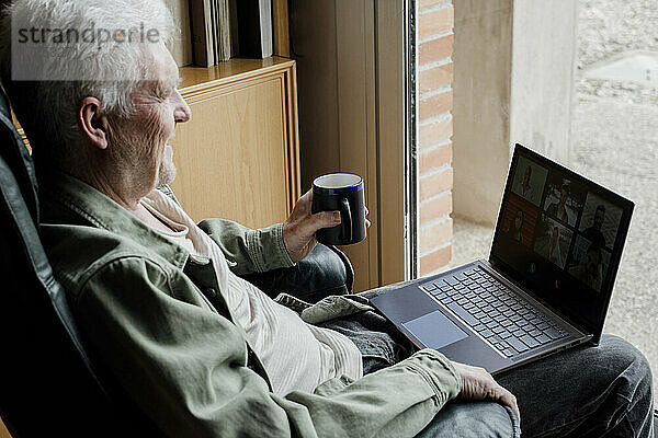 Älterer Mann mit Laptop und Kaffeetasse zu Hause