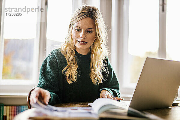 Eine Freiberuflerin liest ein Buch  während sie mit ihrem Laptop im Büro sitzt