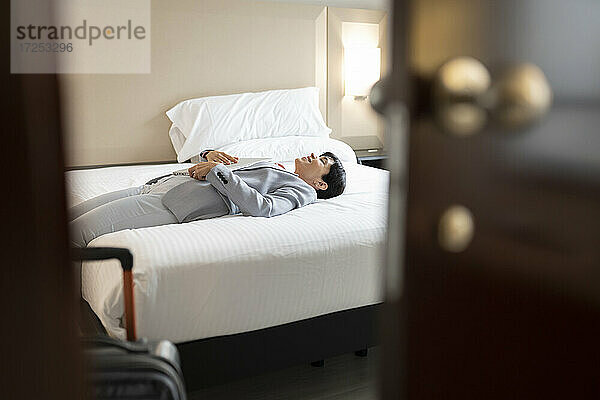 Reife Frau in Businesskleidung auf dem Bett einer Hotelsuite liegend