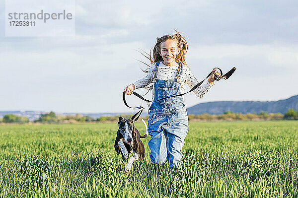 Glückliches Mädchen läuft mit Hund in einem landwirtschaftlichen Feld