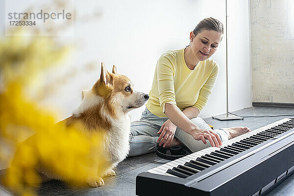 Frau übt Klavier mit Hund  der zu Hause wegschaut