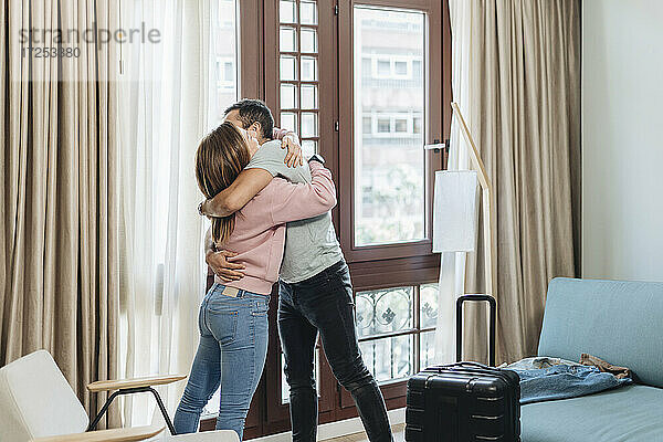 Zärtliches Paar  das sich gegenseitig umarmt  während es am Fenster eines Hotelzimmers steht