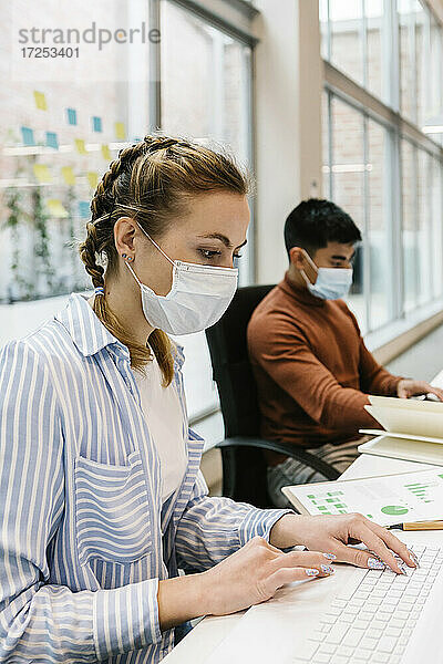 Weibliche Fachkraft nutzt Laptop eines männlichen Kollegen in einem Coworking-Büro während einer Pandemie