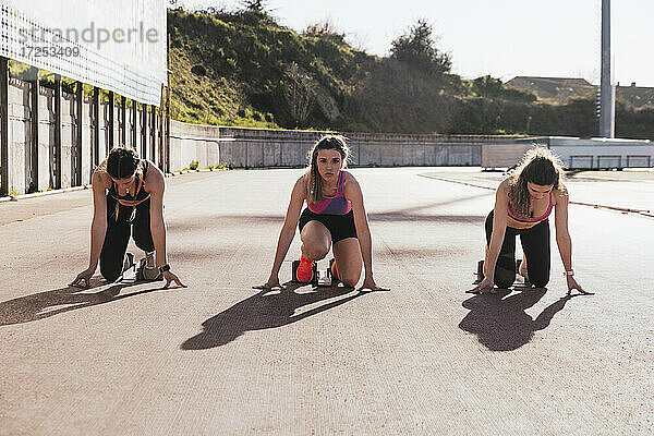 Sportlerinnen kniend bei der Vorbereitung auf ein Rennen an einem sonnigen Tag