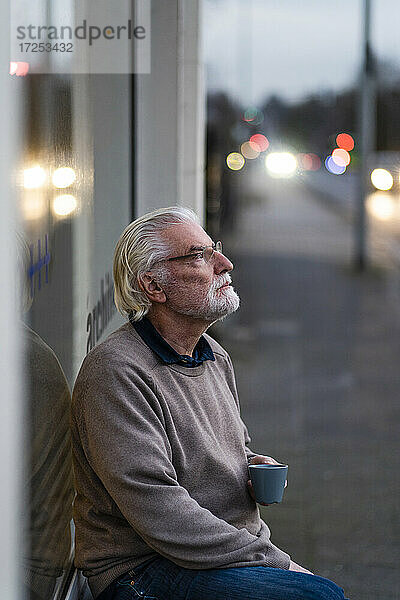 Nachdenklicher älterer Mann sitzt vor einem Straßencafé