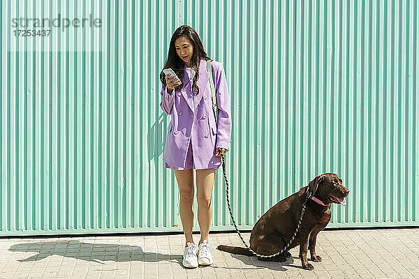 Mittlere erwachsene Frau  die ein Mobiltelefon benutzt und mit einem Hund auf dem Fußweg steht