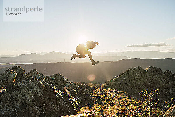 Sportler springt an einem sonnigen Tag auf einen Berg