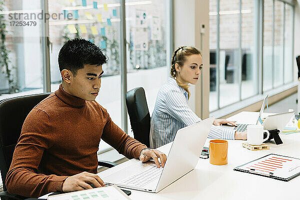 Männlicher Unternehmer  der mit einem Kollegen im Büro am Laptop arbeitet