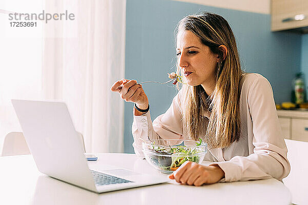 Italien  Frau isst Salat und schaut auf Laptop