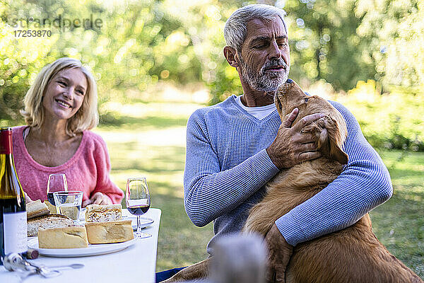 Lächelnde reife Frau  die ihren Mann beim Spielen mit dem Hund im Hinterhof beobachtet