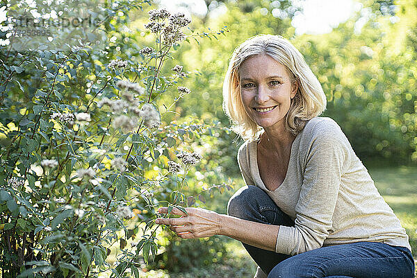 Porträt einer lächelnden reifen Frau  die eine Pflanze im Hinterhof berührt
