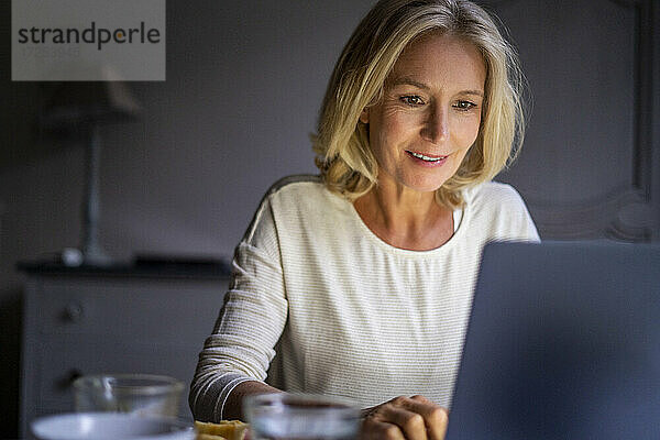 Lächelnde reife Frau benutzt Laptop zu Hause