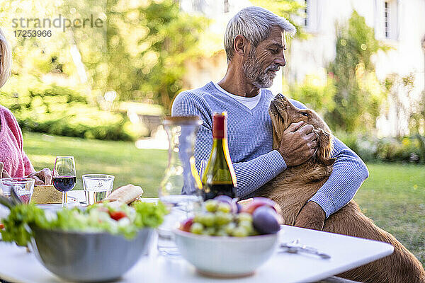 Älterer Mann spielt mit Hund  während er am Tisch sitzt