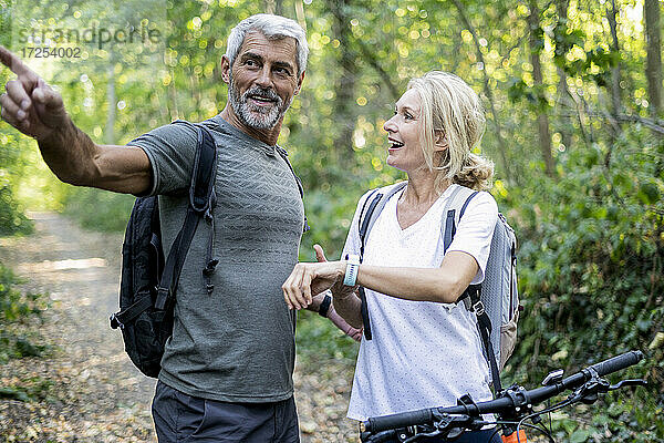Lächelndes reifes Paar  das im Wald die Richtung auf seiner Smartwatch überprüft